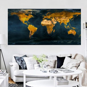 Puede incluir: Una impresión mural rectangular grande que representa un mapa del mundo. Los continentes están representados en tonos dorados y marrones sobre un fondo azul oscuro. La obra de arte se exhibe sobre un sofá blanco, con detalles geográficos.