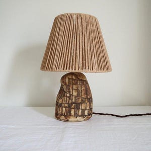 May include: A ceramic table lamp with a brown and white geometric pattern on the base and a natural fibre lampshade.