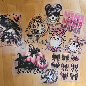 Könnte beinhalten: Eine Sammlung von Halloween-Bügelbildern mit verschiedenen Designs. Enthalten sind Bilder von einem Raben, Totenköpfen, Geistern, Kürbissen, Schleifen und einer schwarzen Katze. Texte beinhalten "Halloween", "Spooky", "Girlie" und "Social Club".