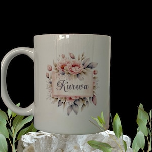 Könnte beinhalten: Weiße Keramiktasse mit einem Blumendesign und dem Wort "Kiruwa" in einem rosa Banner. Die Blumen sind rosa und weiß mit grünen Blättern.