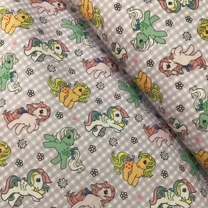 Könnte beinhalten: Lilafarbener und weißer Gingham-Stoff mit einem sich wiederholenden Muster aus bunten Comic-Ponys. Die Ponys sind in verschiedenen Posen und haben unterschiedlich farbige Mähnen und Schwänze.