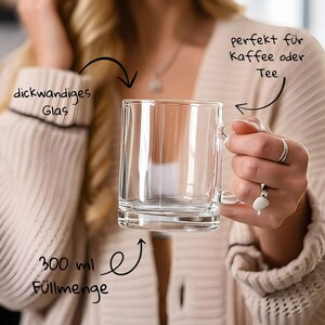 May include: A clear glass mug with a handle, designed for coffee or tea. The mug has a thick-walled design and holds 300 ml. The mug is held by a person wearing a cream-colored sweater.