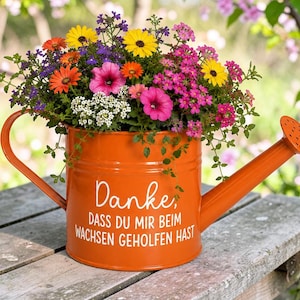Könnte beinhalten: Eine orangefarbene Gießkanne aus Metall, gefüllt mit einem bunten Arrangement aus gelben, rosa, orangefarbenen und weißen Blumen. Auf der Seite steht in weißer Schrift: Danke, DASS DU MIR BEIM WACHSEN GEHOLFEN HAST. Sie hat einen Griff und einen Ausguss.