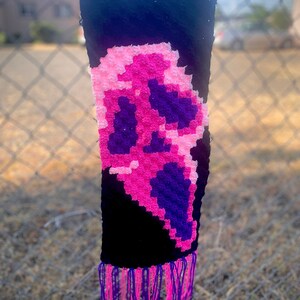 Könnte beinhalten: Ein schwarzer Häkel-Schal mit einem pinkfarbenen und violetten Geister-Design. Der Schal hat Fransen am unteren Ende.