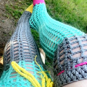 May include: A pair of crocheted thigh-high socks in gray, turquoise, yellow, and pink. The socks are made with a lacy pattern and have a fringe detail at the top.