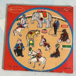 May include: A square wooden peg puzzle featuring a circus theme with illustrations of an elephant, tiger, seal, and performers. The board has red borders, red plastic knobs on each piece, and text including Montrose Products and No. 18-4.