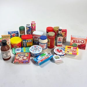 May include: A collection of miniature food and household product replicas including Stubb's barbecue sauce, Old Bay seasoning, Miracle Whip, A1 steak sauce, Jell-O, Bagel Bites, Lunchables, and various other branded containers and boxes arranged together.