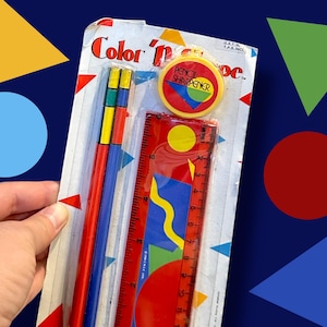 May include: A retro stationery set featuring a red ruler, pencils, and a pencil sharpener. The set is packaged in clear plastic with the words "Color 'n' More". The ruler has a colourful geometric design.