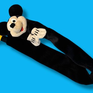 May include: A plush Mickey Mouse head and arms with long black arms and yellow feet. The Mickey Mouse head is cream-colored with a black nose, eyes, and ears, and a red mouth. The gloves are white with black lines.
