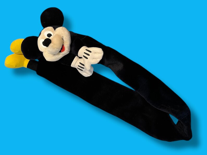 May include: A plush Mickey Mouse head and arms with long black arms and yellow feet. The Mickey Mouse head is cream-colored with a black nose, eyes, and ears, and a red mouth. The gloves are white with black lines.