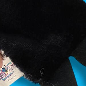 May include: Close-up of a black plush toy with a yellow accent. A tag with a Disney logo is visible. The toy's texture appears soft and fuzzy, suggesting a children's item.