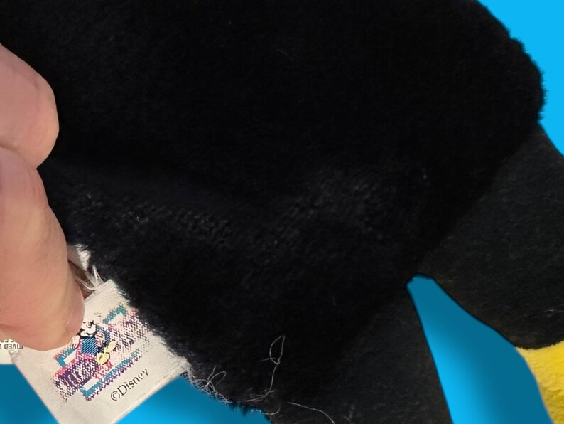 May include: Close-up of a black plush toy with a yellow accent. A tag with a Disney logo is visible. The toy's texture appears soft and fuzzy, suggesting a children's item.