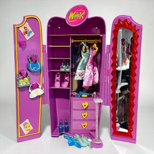 May include: A purple Winx Club doll wardrobe with open doors, revealing a hanging rack with dresses, shelves with shoes, and drawers. The left door has attached purses and a cartoon image. The right door has a mirror.