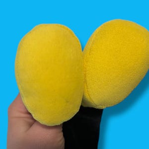 May include: A pair of bright yellow plush ears, possibly part of a costume or toy, against a vibrant blue background. The ears are soft and rounded, with a fuzzy texture. The base of the ears is black.