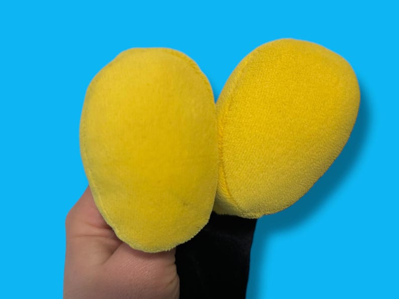 May include: A pair of bright yellow plush ears, possibly part of a costume or toy, against a vibrant blue background. The ears are soft and rounded, with a fuzzy texture. The base of the ears is black.