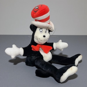 May include: A plush toy of the Cat in the Hat character. The toy is black and white with a red bow tie and a red and white striped hat. The toy has outstretched arms and legs.