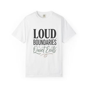 May include: A white short-sleeve t-shirt featuring the black text LOUD BOUNDARIES and the grey script text Quiet Exits. Small light brown hearts are positioned between the words, and a decorative brown line underlines the text.