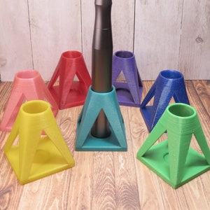 May include: A set of seven colorful triangular stands for holding small tools or accessories. The stands are made of a sparkly plastic material and are arranged in a circle around a black tool with a brown tip.
