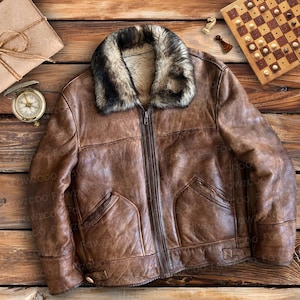 Op de afbeelding: Een bruin leren jack met een nep bontkraag. Het jack heeft een ritssluiting en twee zakken aan de voorkant.