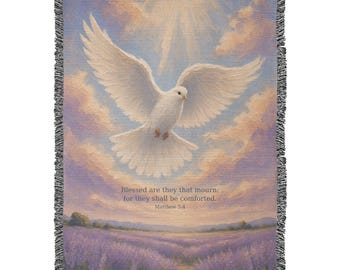 May include: A woven throw blanket featuring a white dove in flight against a sky of soft pink and purple clouds above a lavender field. The text reads: Blessed are they that mourn: for they shall be comforted. Matthew 5:4. Fringed edges.