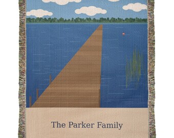 May include: A woven throw blanket featuring a lake scene with a wooden pier extending into blue water, green trees, and white clouds in a blue sky. The bottom section is beige with the text The Parker Family in dark blue lettering.