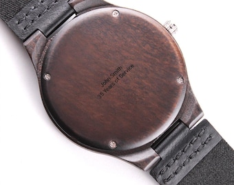 May include: A round wooden wristwatch with a dark brown grain finish and a black leather strap. The back of the watch case is engraved with the text John Smith 35 Years of Service and features four small silver screws around the perimeter.