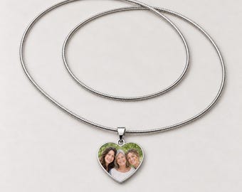 May include: A silver-toned heart-shaped pendant necklace featuring a custom colour photograph of three smiling individuals. The pendant hangs from a thin, flexible silver-toned snake chain, creating a simple and cohesive jewellery piece.