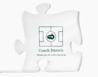May include: A clear acrylic puzzle piece plaque featuring a dark green graphic of a whistle inside a square frame. Below the graphic, the text reads Coach Daniels and Thank you for believing in us in dark green lettering.