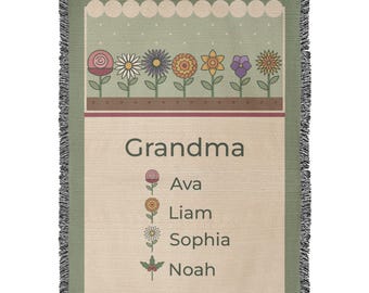 May include: A woven throw blanket with a sage green top section featuring a row of colourful flowers and a cream-coloured bottom section. The text reads Grandma followed by a list of names: Ava, Liam, Sophia, and Noah, each paired with a small flower icon.