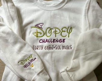 May include: White sweatshirt with green embroidered text that reads "Dopey Challenge forty eight.six miles". The left sleeve has a smaller embroidered design that reads "Dopey 48.6 miles".