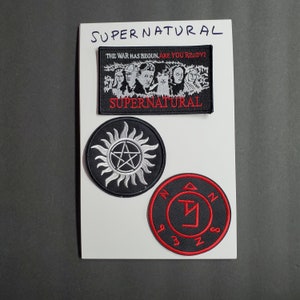 Può includere: Tre toppe ricamate in bianco e nero con le parole "Supernatural" e "The War Has Begun, Are You Ready?" e una stella con un cerchio intorno. C'è anche una toppa ricamata in rosso e nero con un simbolo e le lettere "Z N 3 Z S".