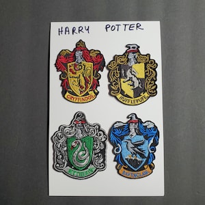 May include: Four embroidered Harry Potter house crests. The crests are on a white background. The crests are for Gryffindor, Hufflepuff, Slytherin, and Ravenclaw. The crests are in their respective house colors.