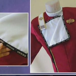 May include: A red and white uniform jacket with gold detailing and a decorative pin. The jacket features a white collar and a white panel with black trim. The uniform is displayed on a mannequin.