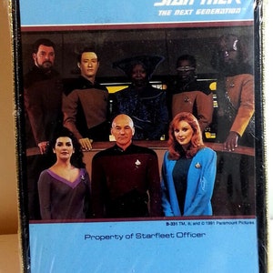 May include: A Star Trek: The Next Generation card with a blue background and a picture of the main cast. The text "Property of Starfleet Officer" is printed on the card.
