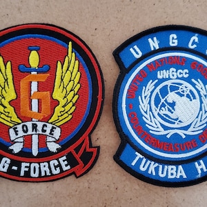 May include: Two embroidered patches, one red with a yellow winged G and the text "G-FORCE", the other blue with a white UN logo and the text "UN GCC - COUNTERMEASURE CENTER - TUKUBA H.Q."