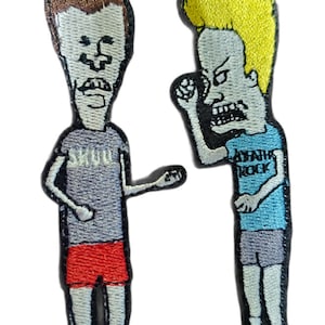 Op de afbeelding: Twee geborduurde strijkpatches met cartoonfiguren uit de animatieserie "Beavis and Butt-Head". De patch links toont Beavis die een grijs shirt draagt met het woord "SHROOM" erop gedrukt, een rode broek en zwarte schoenen. De patch rechts toont Butt-Head die een blauw shirt draagt met de woorden "ASSHOLE ROCK" erop gedrukt, een grijze broek en zwarte schoenen.