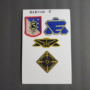 May include: Four embroidered patches featuring the Babylon 5 logo. The patches are on a white background with the text "BABYLON 5" written in black at the top. The patches are in the shape of a shield, a star, a circle, and a diamond. The patches are all in different colors, including red, blue, yellow, and black.