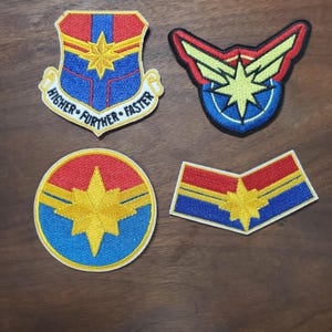 May include: Four embroidered patches featuring a starburst design in red, blue, yellow, and white. One patch has the text "HIGHER • FURTHER • FASTER". The patches are in various shapes, including a shield, a circle, and a stylized emblem.