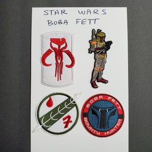 Pode incluir: Quatro patches bordados com o personagem de Star Wars Boba Fett. Os patches são brancos, verdes e azuis com detalhes vermelhos e pretos. Os patches apresentam o símbolo mandaloriano, o capacete de Boba Fett e o texto "BOBA FETT BOUNTY HUNTER".