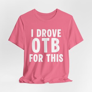 May include: A pink t-shirt with the white text "I DROVE OTB FOR THIS". The shirt has short sleeves and a crew neck. The text is centered on the front of the shirt.