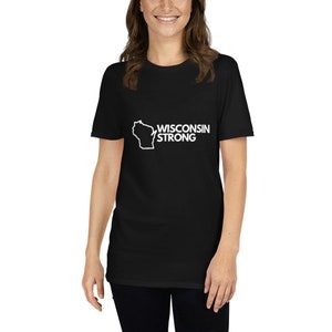 Peut inclure: T-shirt noir avec le contour blanc du Wisconsin et l'inscription "WISCONSIN STRONG". Le t-shirt est à col rond et à manches courtes.