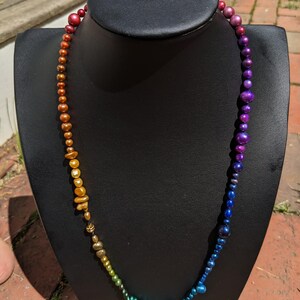 Pode incluir: Um colar degrad&ecirc; arco-&iacute;ris feito de contas iridescentes. O colar est&aacute; em um busto de manequim preto.