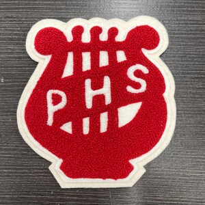 Könnte beinhalten: Ein rot-weißes Filz-Patch mit den weißen Buchstaben "PHS". Das Patch hat ein strukturiertes, flauschiges Aussehen und einen weißen Rand. Das Design ist eine stilisierte Leierform, die oft mit Musik in Verbindung gebracht wird.