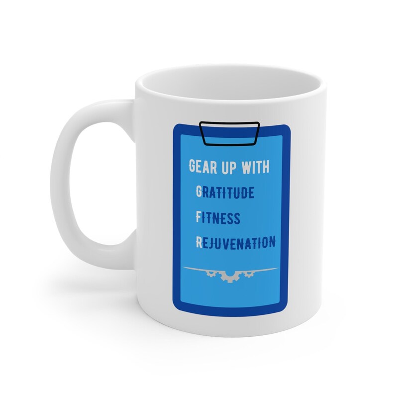 May include: White ceramic mug with a blue and white graphic of a clipboard with the text "Gear Up With Gratitude Fitness Rejuvenation".