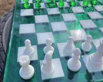 May include: A clear green and white chess set. The board is transparent green with white squares. The chess pieces are white and translucent green. The pieces are arranged on the board, ready for play.