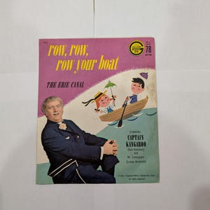 Puede incluir: Portada de álbum de disco vintage con el título "Row, Row, Row Your Boat" y "The Erie Canal". La portada es rosa y presenta a Captain Kangaroo, ilustraciones de niños en un bote y un hombre con un traje azul. El disco reproduce a 78 RPM.