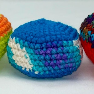May include: Three handmade crochet balls in vibrant colors. One is lime green with orange stripes, another is blue with white and turquoise accents, and the third is red with a multicolored stripe. These soft balls are ideal for juggling or play.