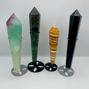 May include: Four crystal points on black metal stands. The crystals are green, black, orange, and light green.