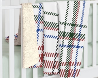 Könnte beinhalten: Eine weiße Decke mit einem Karomuster aus roten, grünen und blauen Streifen. Die Decke hat ein weiches, cremefarbenes Sherpa-Futter. Die Decke ist über einem weißen Gitterbettgeländer drapiert.