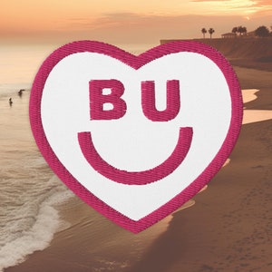 Puede incluir: Un parche de corazón rosa con fondo blanco y las letras "BU" en blanco en su interior. El parche tiene una boca sonriente blanca.